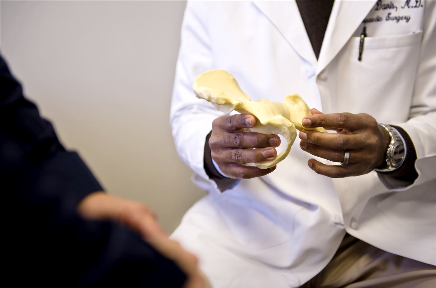 A PrimeOrtho surgeon holding an anatomical model while talking a patient through it